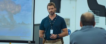 Movie still from “Chappie” (2015), directed by Neill Blomkamp – A man in a blue shirt is holding a gun; Medium shot, Over the shoulder angle