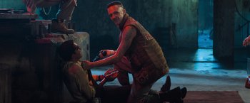 Movie still from “Chappie” (2015), directed by Neill Blomkamp – A man in a vest is holding a microphone; Medium shot, Over the shoulder angle