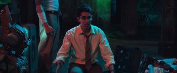 Movie still from “Chappie” (2015), directed by Neill Blomkamp – A man sitting on a chair wearing a tie; Medium shot, High angle