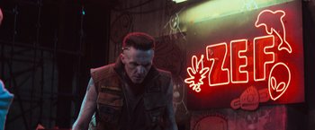 Movie still from “Chappie” (2015), directed by Neill Blomkamp – A man with a mohawk haircut standing in front of a neon sign; Medium shot, Low angle