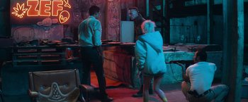 Movie still from “Chappie” (2015), directed by Neill Blomkamp – A group of people standing in a room with graffiti on the walls; Wide shot, Over the shoulder angle