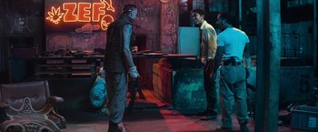 Movie still from “Chappie” (2015), directed by Neill Blomkamp – A group of men standing around in a room; Wide shot, Over the shoulder angle