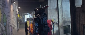 Movie still from “Chappie” (2015), directed by Neill Blomkamp – A man in a suit and helmet standing in front of a wall; Medium shot, Over the shoulder angle