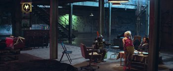 Movie still from “Chappie” (2015), directed by Neill Blomkamp – A man sitting on a chair in a room with graffiti on the walls; Wide shot, High angle
