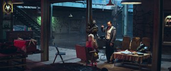 Movie still from “Chappie” (2015), directed by Neill Blomkamp – A man and a woman are in a room with graffiti on the walls; Wide shot, Over the shoulder angle