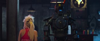 Movie still from “Chappie” (2015), directed by Neill Blomkamp – A woman standing in front of a large robot; Medium shot, Over the shoulder angle