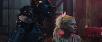 Movie still from “Chappie” (2015), directed by Neill Blomkamp – A woman in a blonde pony tail and a robot with long blonde hair; Close Up shot, Over the shoulder angle