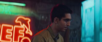 Movie still from “Chappie” (2015), directed by Neill Blomkamp – A young man wearing glasses and a tan shirt; Close Up shot, Over the shoulder angle