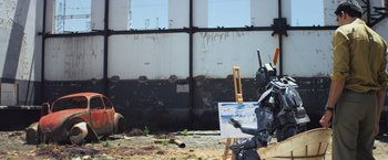 Movie still from “Chappie” (2015), directed by Neill Blomkamp – An image of a robot painting a picture outside; Wide shot, Over the shoulder angle
