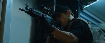 Movie still from “Chappie” (2015), directed by Neill Blomkamp – A man holding a rifle in a room; Close Up shot, Low angle