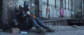 Movie still from “Chappie” (2015), directed by Neill Blomkamp – A robot sitting on the ground in front of a man; Wide shot, Low angle