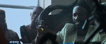 Movie still from “Chappie” (2015), directed by Neill Blomkamp – A man sitting in front of another man holding a cell phone; Medium shot, Low angle