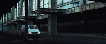 Movie still from “Chappie” (2015), directed by Neill Blomkamp – A white car parked in a parking lot next to a building; Extreme Wide shot, Low angle