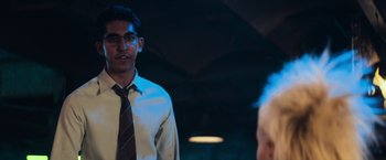 Movie still from “Chappie” (2015), directed by Neill Blomkamp – A young man wearing a tie and glasses in the dark; Medium shot, Over the shoulder angle