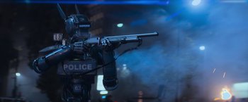 Movie still from “Chappie” (2015), directed by Neill Blomkamp – A police officer is holding a gun in his hand; Medium shot, Low angle