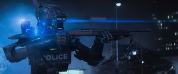 Movie still from “Chappie” (2015), directed by Neill Blomkamp – A police officer is holding a gun in the dark; Medium shot, Low angle