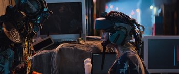 Movie still from “Chappie” (2015), directed by Neill Blomkamp – A person wearing a helmet and holding a tablet; Medium shot, Over the shoulder angle