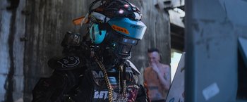 Movie still from “Chappie” (2015), directed by Neill Blomkamp – A robot with a man in the background looking at him; Close Up shot, Over the shoulder angle