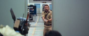 Movie still from “Chappie” (2015), directed by Neill Blomkamp – A man in a tan shirt is holding a remote control; Medium shot, Over the shoulder angle