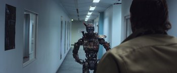 Movie still from “Chappie” (2015), directed by Neill Blomkamp – A man is standing next to a robot in a hallway; Wide shot, Over the shoulder angle