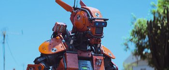 Movie still from “Chappie” (2015), directed by Neill Blomkamp – An image of an orange and black robot in the sky; Medium shot, Low angle