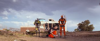 Movie still from “Chappie” (2015), directed by Neill Blomkamp – A man sitting on the ground next to two robots; Extreme Wide shot, Low angle
