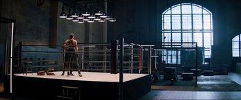Movie still from “Charlie's Angels” (2019), directed by Elizabeth Banks – A man standing in a boxing ring in front of a window; Wide shot, High angle