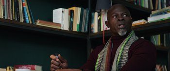 Movie still from “Charlie's Angels” (2019), directed by Elizabeth Banks – A man sitting in front of a book shelf holding a cell phone; Close Up shot, Low angle