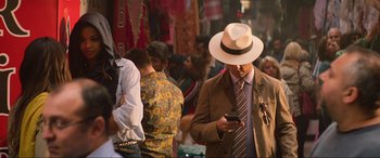 Movie still from “Charlie's Angels” (2019), directed by Elizabeth Banks – A man in a hat and a suit looking at his cell phone; Wide shot, Low angle