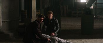 Movie still from “Charlie's Angels” (2019), directed by Elizabeth Banks – Two men sitting on the ground next to each other; Medium shot, Over the shoulder angle