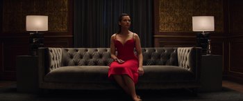 Movie still from “Charlie's Angels” (2019), directed by Elizabeth Banks – A woman in a red dress is sitting on a couch; Wide shot, Low angle