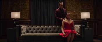 Movie still from “Charlie's Angels” (2019), directed by Elizabeth Banks – A woman in a red dress sitting on a couch next to a man in a black suit; Medium shot, Low angle