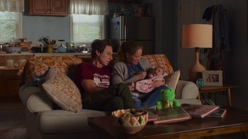 Movie still from “Cheaper by the Dozen” (2022), directed by Gail Lerner – A man , woman , and a baby sitting on a couch; Medium shot, High angle