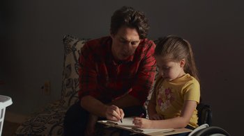 Movie still from “Cheaper by the Dozen” (2022), directed by Gail Lerner – A man sitting next to a little girl writing on a piece of paper; Medium shot, Over the shoulder angle