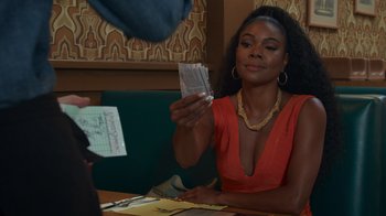 Movie still from “Cheaper by the Dozen” (2022), directed by Gail Lerner – A woman sitting at a table holding a stack of money; Close Up shot, Over the shoulder angle