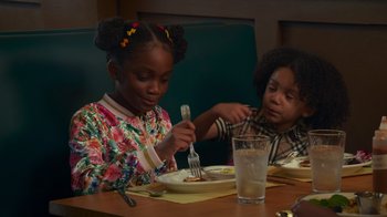 Movie still from “Cheaper by the Dozen” (2022), directed by Gail Lerner – Two young children sitting at a table eating food; Medium shot, Over the shoulder angle