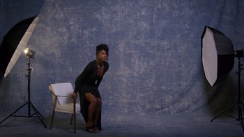 Movie still from “Cheaper by the Dozen” (2022), directed by Gail Lerner – A woman sitting on top of a chair in front of a wall; Wide shot, High angle