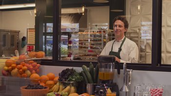 Movie still from “Cheaper by the Dozen” (2022), directed by Gail Lerner – A man standing in front of a display of fruits and vegetables; Medium shot, Over the shoulder angle