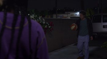 Movie still from “Cheaper by the Dozen” (2022), directed by Gail Lerner – A man holding a ball in his hand while standing next to a wall; Wide shot, Over the shoulder angle