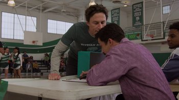 Movie still from “Cheaper by the Dozen” (2022), directed by Gail Lerner – Two men looking at a book on top of a table; Medium shot, Over the shoulder angle