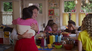 Movie still from “Cheaper by the Dozen” (2022), directed by Gail Lerner – A man and a woman hugging at a table with a group of children; Medium shot, Over the shoulder angle