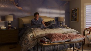 Movie still from “Cheaper by the Dozen” (2022), directed by Gail Lerner – A man laying on a bed under a comforter; Wide shot, High angle