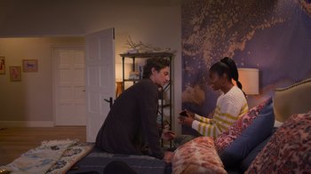 Movie still from “Cheaper by the Dozen” (2022), directed by Gail Lerner – Two people sitting on a bed looking at a phone; Medium shot, High angle