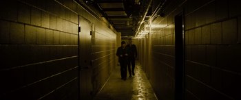 Movie still from “Enemy” (2013), directed by Denis Villeneuve – Two men are walking down a hallway in a building; Wide shot, High angle