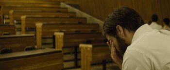 Movie still from “Enemy” (2013), directed by Denis Villeneuve – A man sitting in front of a bunch of wooden benches; Close Up shot, High angle