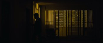 Movie still from “Enemy” (2013), directed by Denis Villeneuve – A man standing next to a window in a room; Extreme Wide shot, High angle