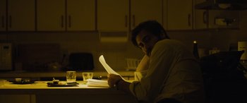 Movie still from “Enemy” (2013), directed by Denis Villeneuve – A man sitting at a kitchen table reading a paper; Medium shot, Low angle