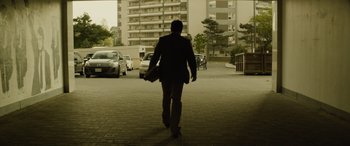 Movie still from “Enemy” (2013), directed by Denis Villeneuve – A man walking down a street holding a briefcase; Wide shot, Low angle