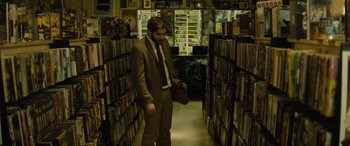 Movie still from “Enemy” (2013), directed by Denis Villeneuve – A man wearing a suit and tie in a library; Medium shot, High angle