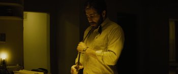 Movie still from “Enemy” (2013), directed by Denis Villeneuve – A man in a yellow shirt is tying a tie; Medium shot, Low angle